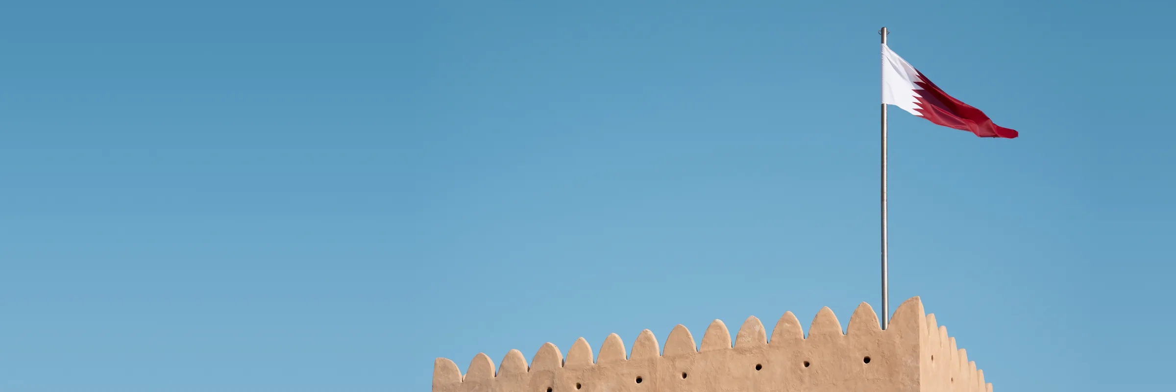 The Qatar flag flying over the wall of a heritage fort